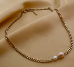 Close-up of a model wearing a dainty gold curb chain necklace featuring a pink baroque pearl and a small champagne pearl, styled with an ivory silk top