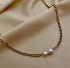 Close-up of a dainty gold curb chain necklace featuring a pink baroque pearl and a small champagne pearl, styled with an ivory silk top