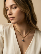 Elegant gold chain necklace with a round black pearl pendant worn by a woman in an ivory silk blouse. Editorial jewelry photography