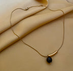 Elegant gold curved bar necklace with black pearl pendant worn by a model. Minimalist jewelry design featuring a high-luster round black pearl and sleek gold spacer on a delicate chain.