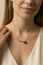Elegant gold curved bar necklace with black pearl pendant worn by a model. Minimalist jewelry design featuring a high-luster round black pearl and sleek gold spacer on a delicate chain