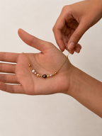Gold chain bracelet displayed across the hand with a central grey pearl, pale pearls and polished gold beads