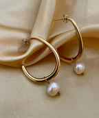 Close-up of a gold hoop earring with a single white pearl drop, highlighting the metallic luster and pearl detail against a soft neutral background