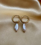 Close-up photography of a dainty gold hoop earring featuring a lustrous white baroque pearl drop. High-resolution commercial jewelry shot showcasing organic keshi pearl texture, nacre iridescence, and a simple gold clasp against a matte ivory background.