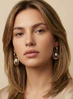 Close-up editorial photography of a gold hoop drop earring featuring a suspended white high-luster pearl, worn by a model with blonde-brown hair against a matte ivory background. High-resolution luxury jewelry shot highlighting realistic gold texture and pearl iridescence.
