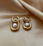 Close-up editorial photography of a gold hoop drop earring featuring a suspended white high-luster pearl