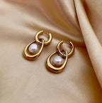 Close-up editorial photography of a gold hoop drop earring featuring a suspended white high-luster pearl