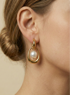 Close-up editorial photography of a gold hoop drop earring featuring a suspended organic white high-luster pearl. High-resolution luxury jewelry shot highlighting realistic gold texture and pearl iridescence.