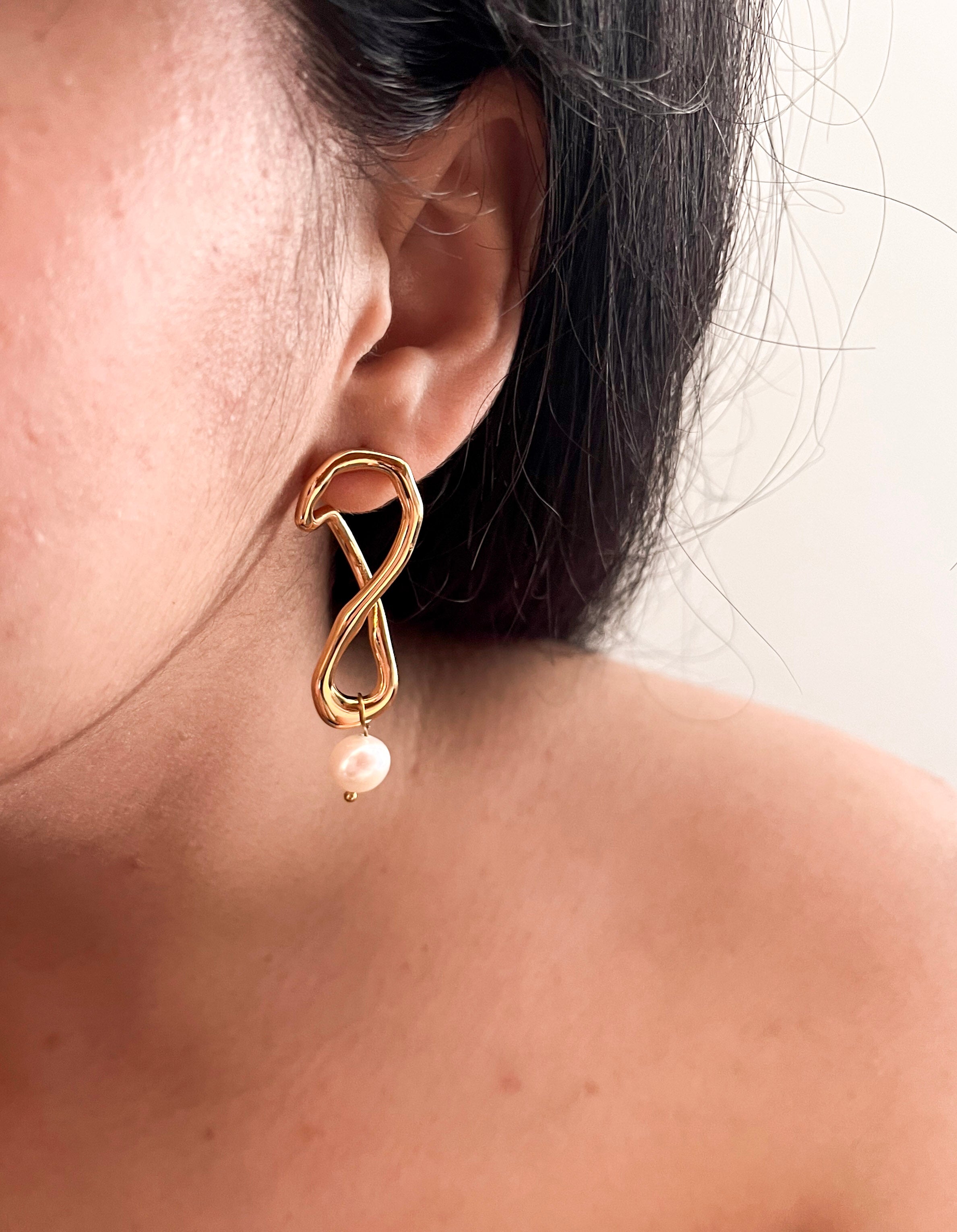 Close-up of a gold knot earring with a white baroque freshwater pearl drop worn on the ear.