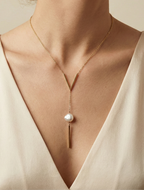 Close-up of a gold lariat necklace featuring a geometric V-shaped bar and a single white baroque pearl drop on a delicate chain