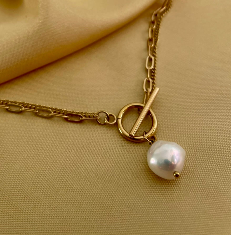 Close-up detail of a double-strand gold chain necklace featuring a lustrous white baroque pearl pendant and a T-bar toggle clasp