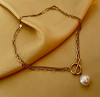 Close-up detail of a double-strand gold chain necklace featuring a lustrous white baroque pearl pendant and a T-bar toggle clasp