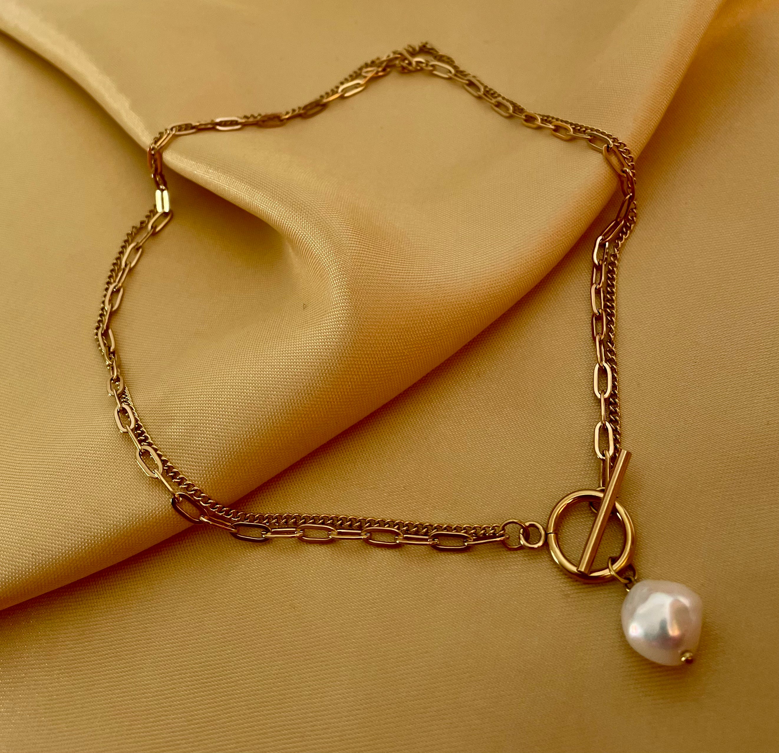 Close-up detail of a double-strand gold chain necklace featuring a lustrous white baroque pearl pendant and a T-bar toggle clasp
