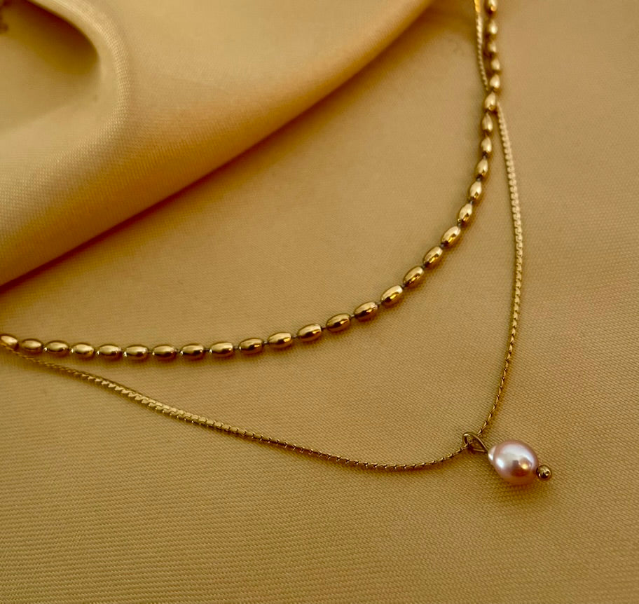 layered gold necklace set featuring a choker with small gold beads and a delicate chain with a single dark pink oval pearl pendant
