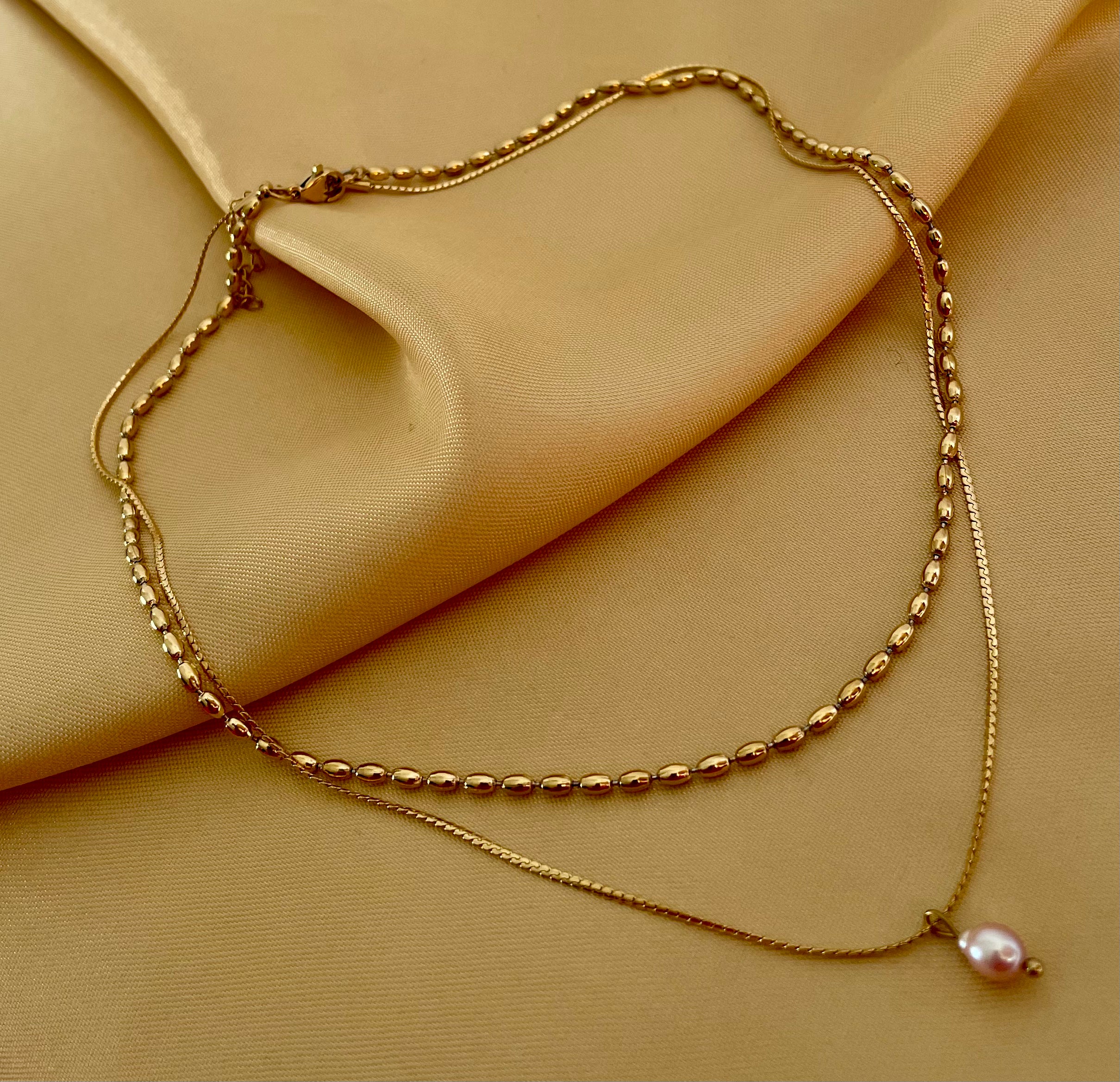 layered gold necklace set featuring a choker with small gold beads and a delicate chain with a single dark pink oval pearl pendant