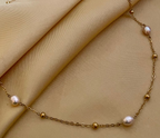 Close-up of a dainty gold chain necklace featuring three small, oval champagne pearls and gold spacer beads
