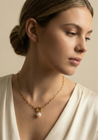 Elegant jewelry photography close-up showing a chunky gold link necklace with a pearl drop, worn by a model with a deep-neck silk blouse.