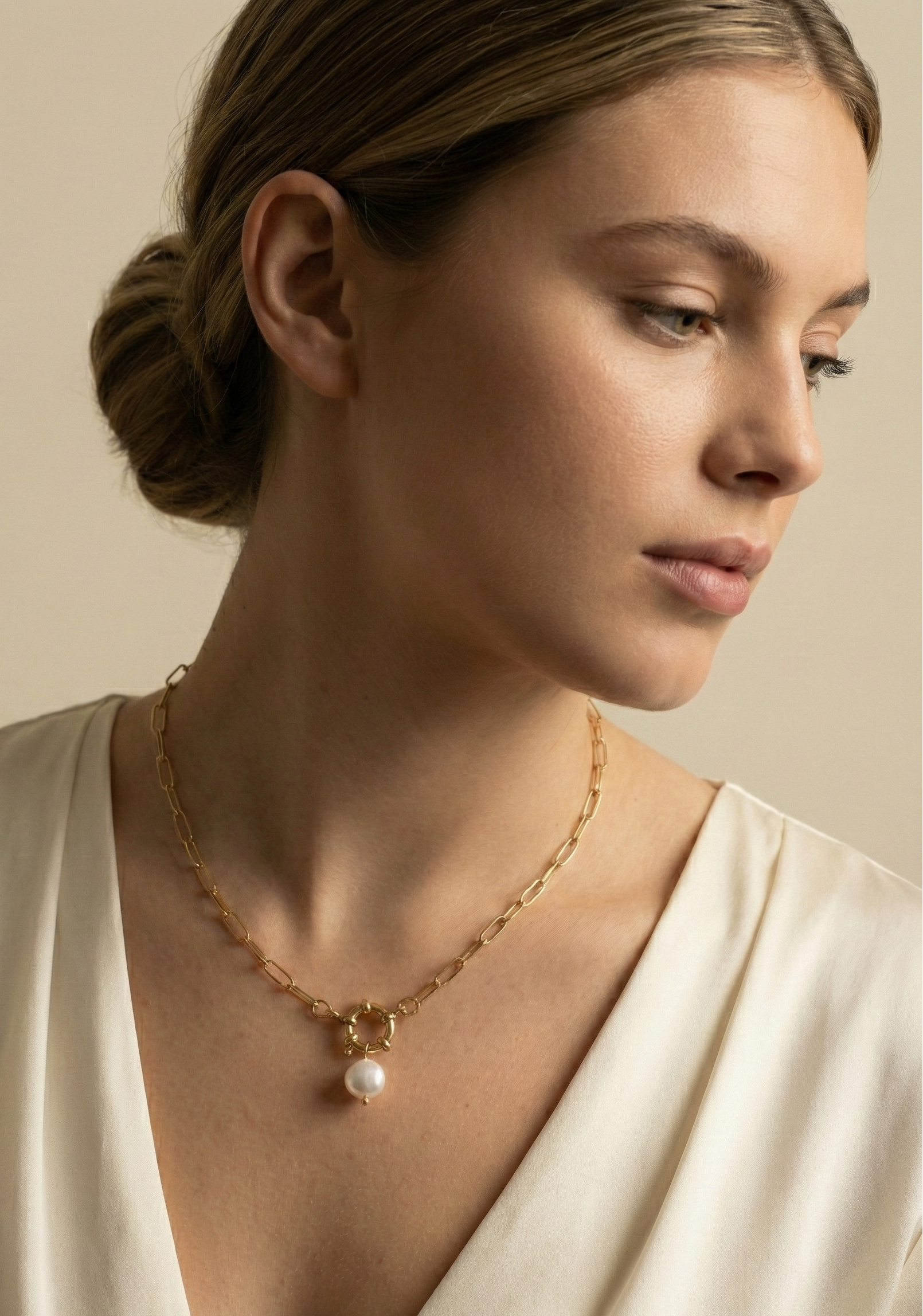 Elegant jewelry photography close-up showing a chunky gold link necklace with a pearl drop, worn by a model with a deep-neck silk blouse.