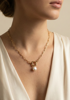 Close-up of a woman's neck wearing a gold link chain necklace with a front-facing toggle closure and a single white baroque pearl charm.