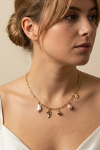 Model wearing a gold paperclip chain necklace featuring a white keshi pearl, gold dolphin charm, pink baroque pearl, and gold sunflower charm