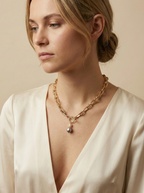 Detail shot of a luxury gold link necklace worn on an ivory silk top. The focal point is a T-bar toggle closure holding a high-shine metallic grey baroque pearl and a champagne oval pearl, showing deep luster and smooth nacre