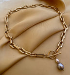 Detail shot of a luxury gold link necklace. The focal point is a T-bar toggle closure holding a high-shine metallic grey baroque pearl and a champagne oval pearl, showing deep luster and smooth nacre