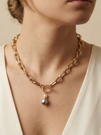 Detail shot of a luxury gold link necklace worn on an ivory silk top. The focal point is a T-bar toggle closure holding a high-shine metallic grey baroque pearl and a champagne oval pearl, showing deep luster and smooth nacre
