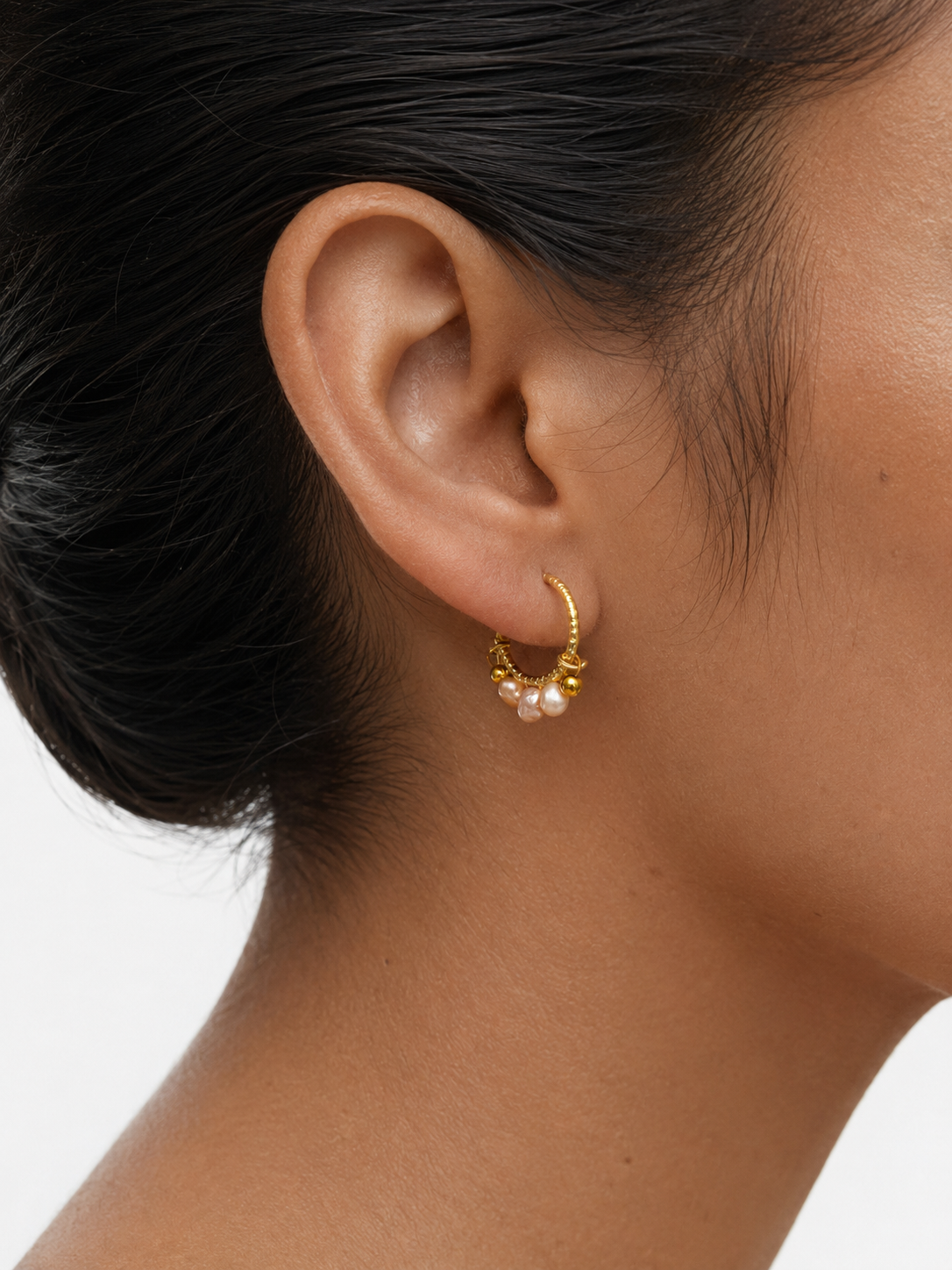 Woman wearing a gold creole hoop earring with pink and gold baroque freshwater pearls and polished gold beads.
