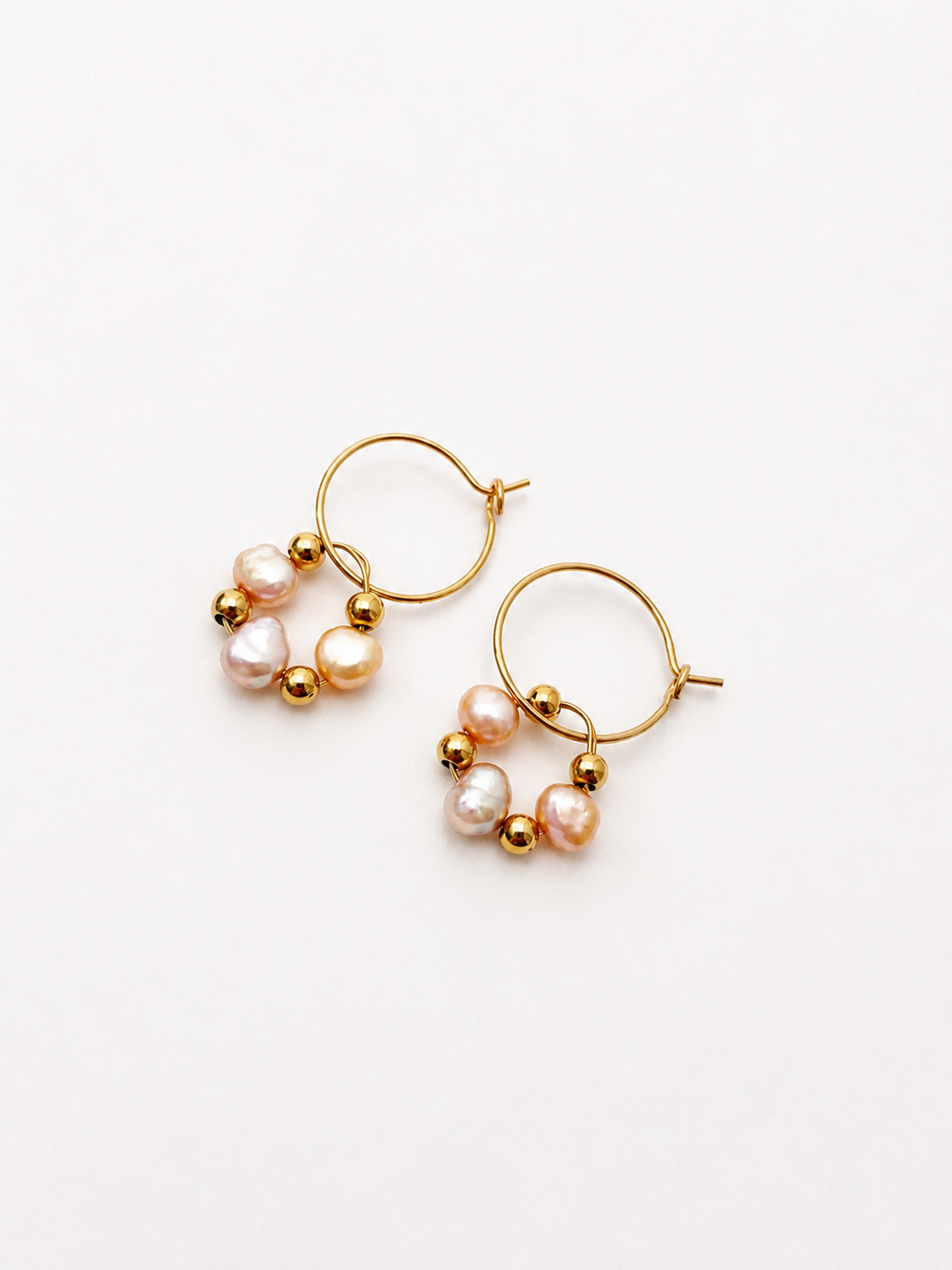 Angled view of gold hoop earrings with gold and pink baroque freshwater pearls and polished gold beads