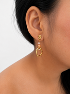 Close-up of a sculptural gold droplet earring with gold and pink baroque freshwater pearls worn on the ear