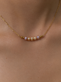 Close-up of a gold necklace with 4 mm pink and gold Keshi freshwater pearls worn on the neck.