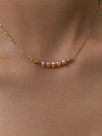 Close-up of a gold necklace with 4 mm pink and gold Keshi freshwater pearls worn on the neck.