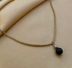 Close-up of a gold rope chain necklace featuring a pendant with a round black pearl and a small grey baroque pearl