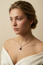 Close-up of a gold rope chain necklace featuring a pendant with a round black pearl and a small grey baroque pearl, worn by a model in an ivory silk top