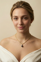 Close-up of a gold rope chain necklace featuring a pendant with a round black pearl and a small grey baroque pearl, worn by a model in an ivory silk top