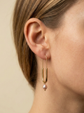 Close-up of a model wearing modern gold safety pin drop earrings featuring a lustrous pink oval pearl charm. Minimalist gold wire earrings with a U-shape design and natural pearl detail
