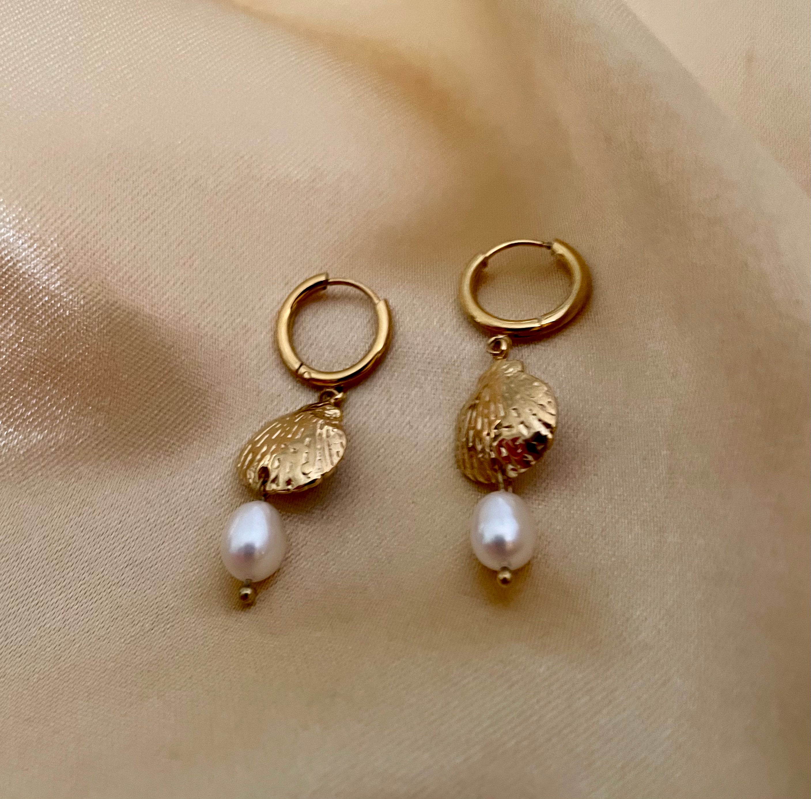 Close-up detail of gold scallop shell earrings featuring a lustrous white pearl drop