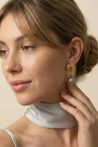 Close-up side profile of a brunette model with a low bun wearing gold concentric spiral statement earrings with a lustrous organic freshwater grey pearl drop