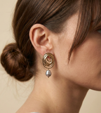 Close-up side profile of a brunette model with a low bun wearing gold concentric spiral statement earrings with a lustrous organic freshwater grey pearl drop