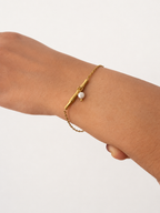 Gold chain bracelet with a sculpted twig bar and pale grey pearl drop on the wrist