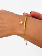 Gold chain bracelet with a sculpted twig bar and white freshwater pearl drop on the wrist