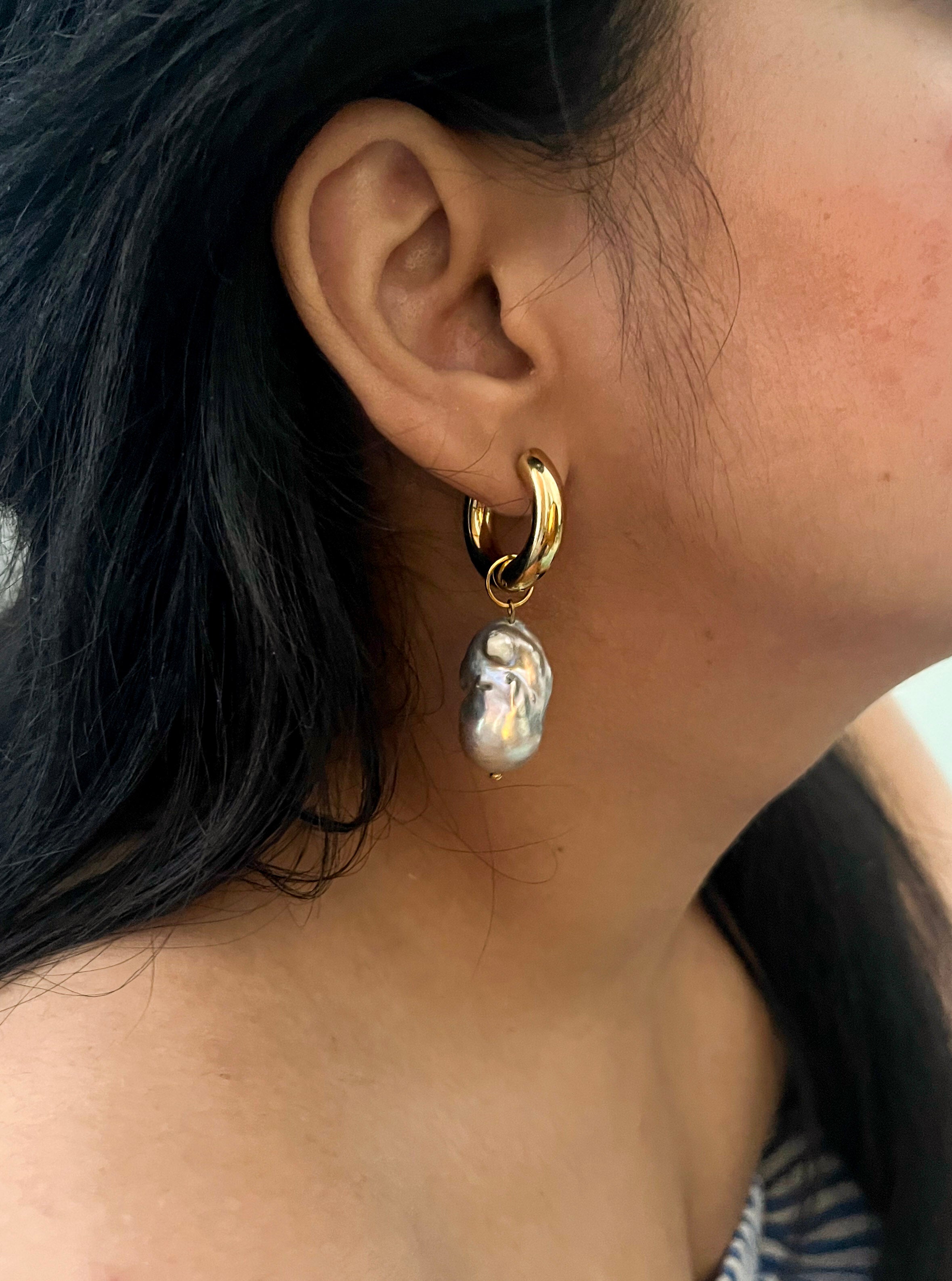 Close-up of a chunky gold hoop earring with a sculptural grey baroque freshwater pearl worn on the ear