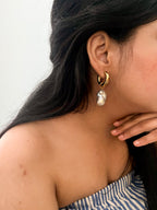Woman wearing a chunky gold hoop earring with a large grey baroque freshwater pearl drop.