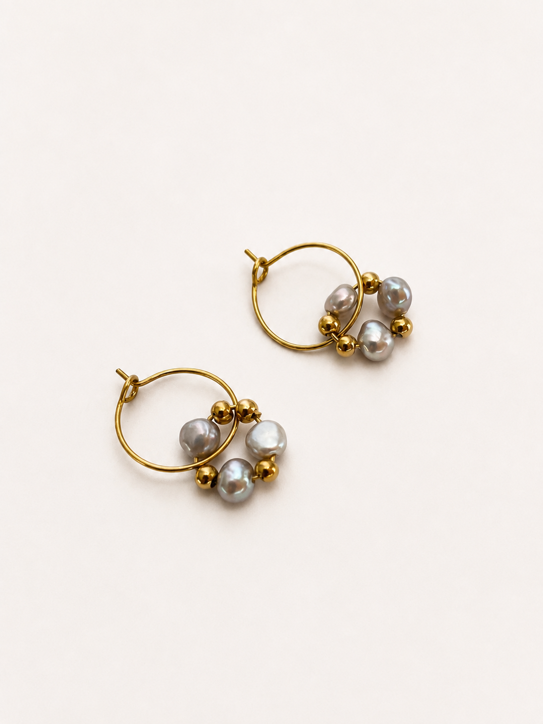 Angled view of gold hoop earrings with grey baroque freshwater pearls and polished gold bead accents