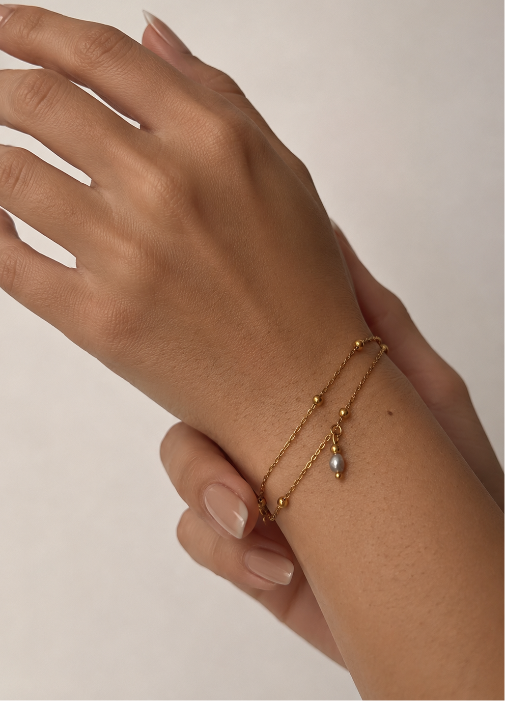 Close-up of a gold double-chain bracelet with polished beads and a grey baroque freshwater pearl drop