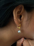 Close-up of a gold drop earring with a grey baroque freshwater pearl worn on the ear.