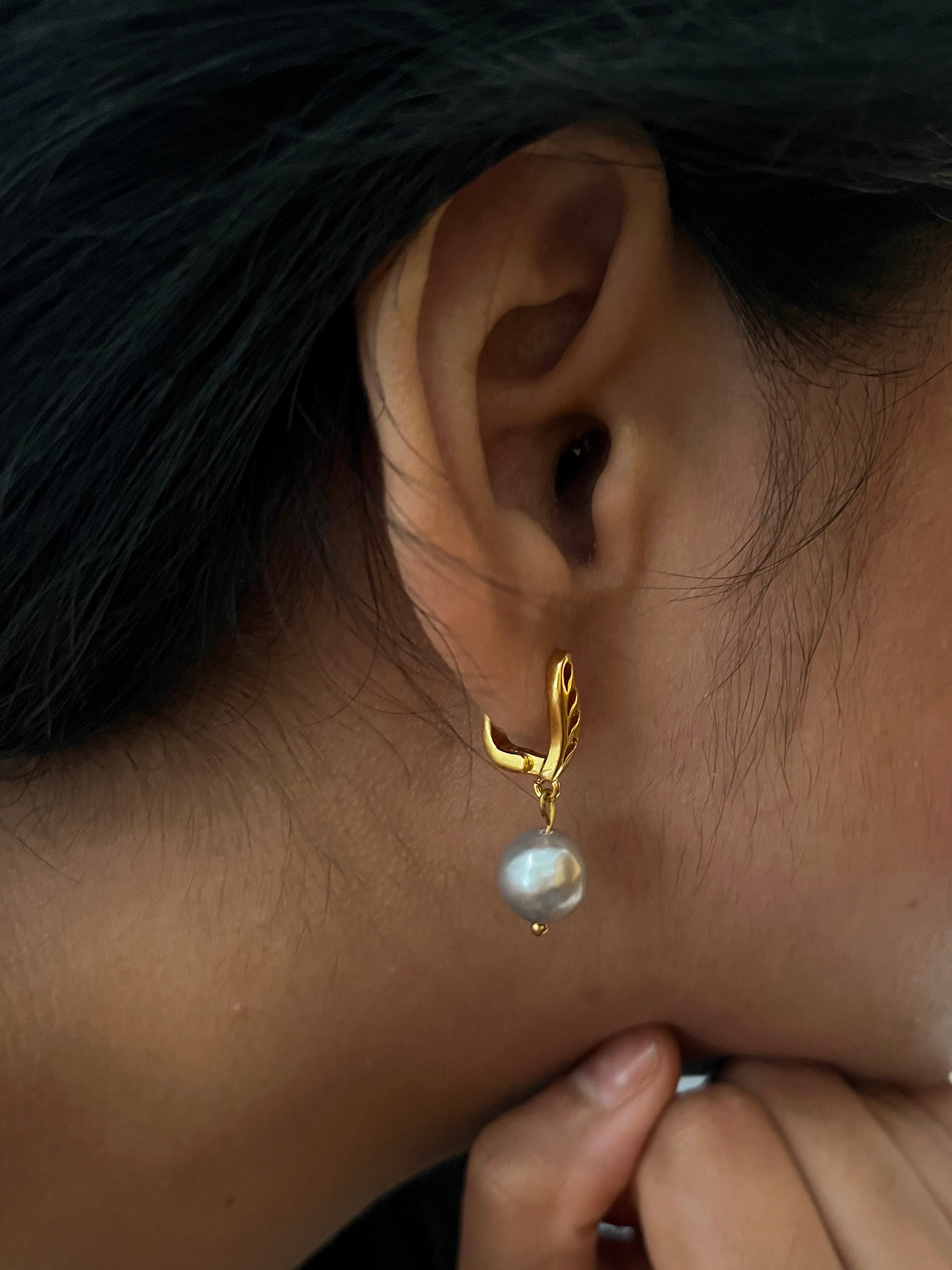 Close-up of a gold drop earring with a grey baroque freshwater pearl worn on the ear.