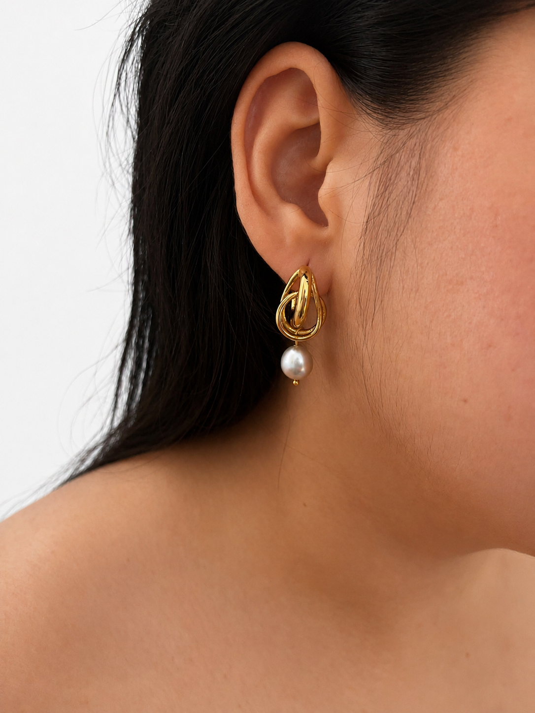 Close-up of a gold droplet earring with a grey baroque freshwater pearl drop worn on the ear.