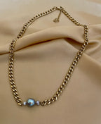 Gold curb chain necklace with a central grey baroque pearl. The pearl has a silvery luster.