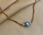 Close-up detail of an organic shaped grey pearl pendant on a gold curb chain, highlighting the iridescent nacre and handmade craftsmanship